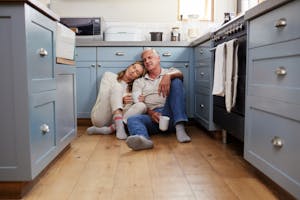 Senior couple sitting on kitchen floor reviewing financial documents together