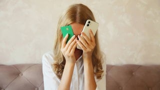 Eine junge Frau hält eine Kreditkarte und ein Handy vors Gesicht