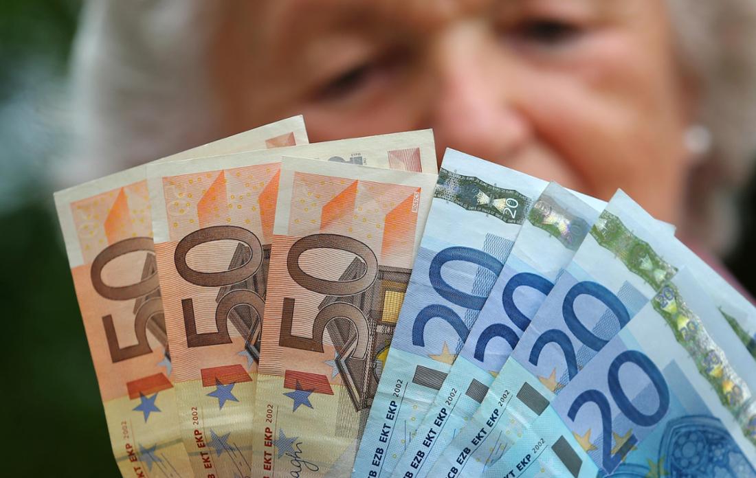 A retiree holds various euro bills in her hands