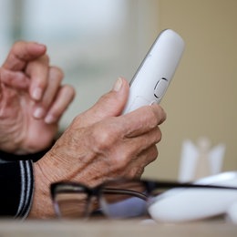 Foto: Hände einer älteren Person halten ein schnurloses Festnetztelefon.