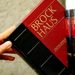 Hand zieht Brockhaus-Lexikon-Band aus einem Regal.