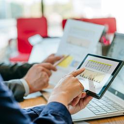 Two people examining financial data on tablets and laptops illustrating long term investment comparison