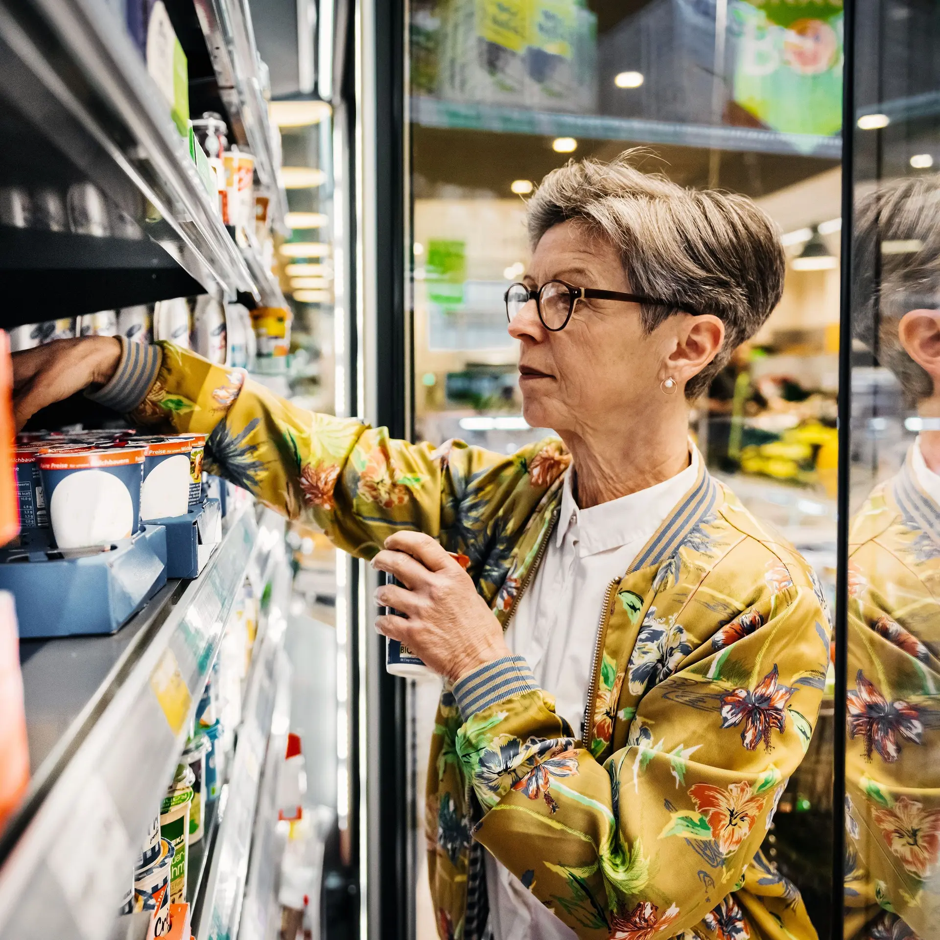 Eine ältere Frau im Supermarkt, die Lebensmittel aus einem Kühlschrank herausholt