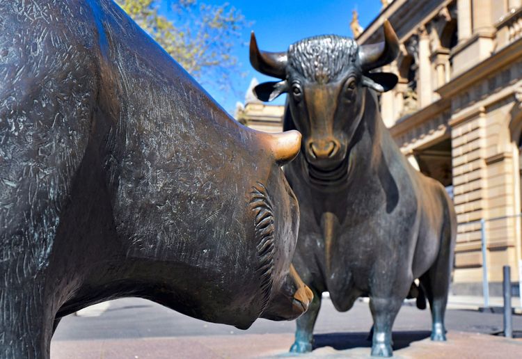 Bronze statues of bull and bear in front of Frankfurt Stock Exchange on sunny weather, symbolizing rising and falling stock markets