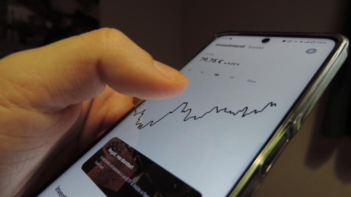 Hand hält Smartphone mit Aktienchart und Finanzdaten