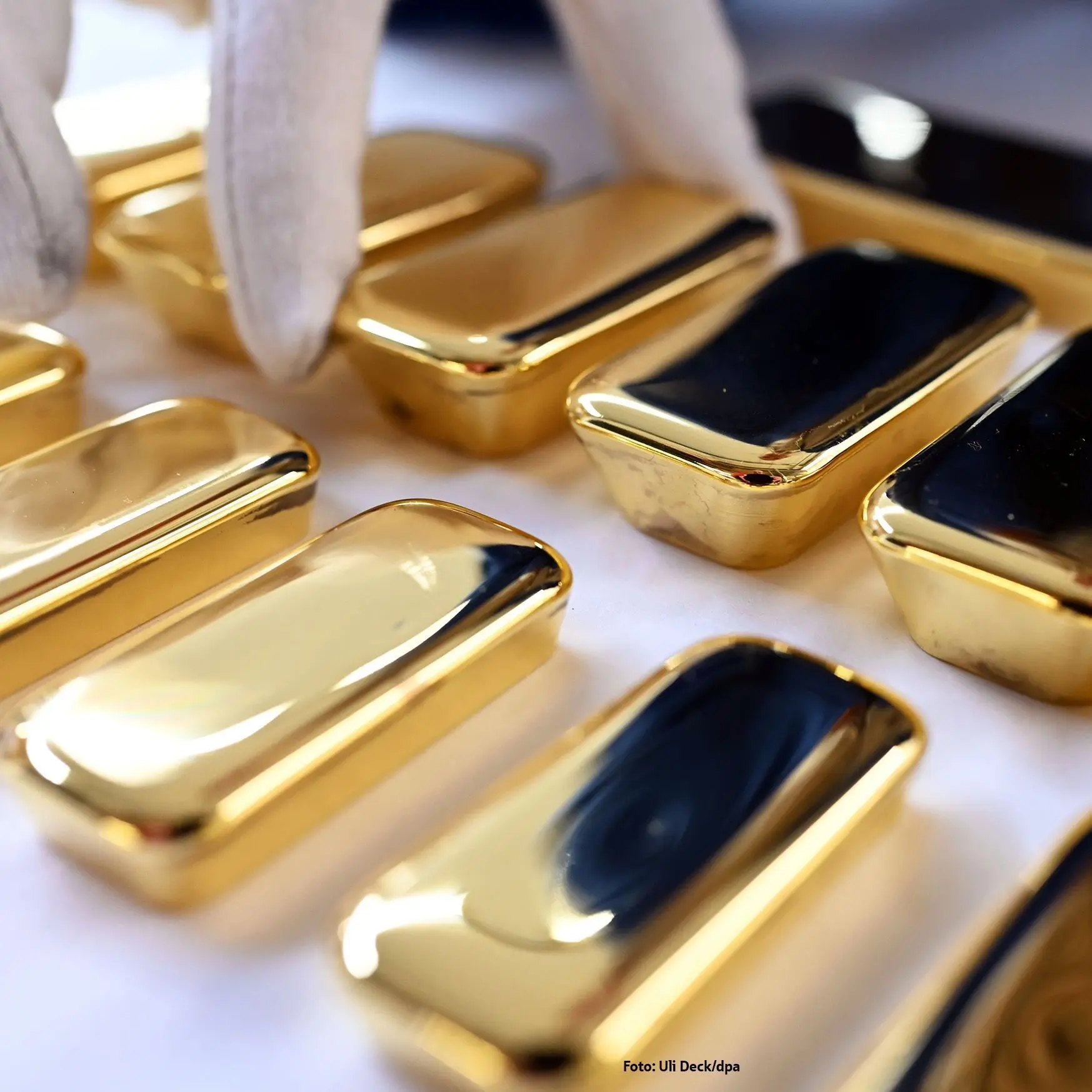 A hand wearing a white cotton glove sorting gold bars